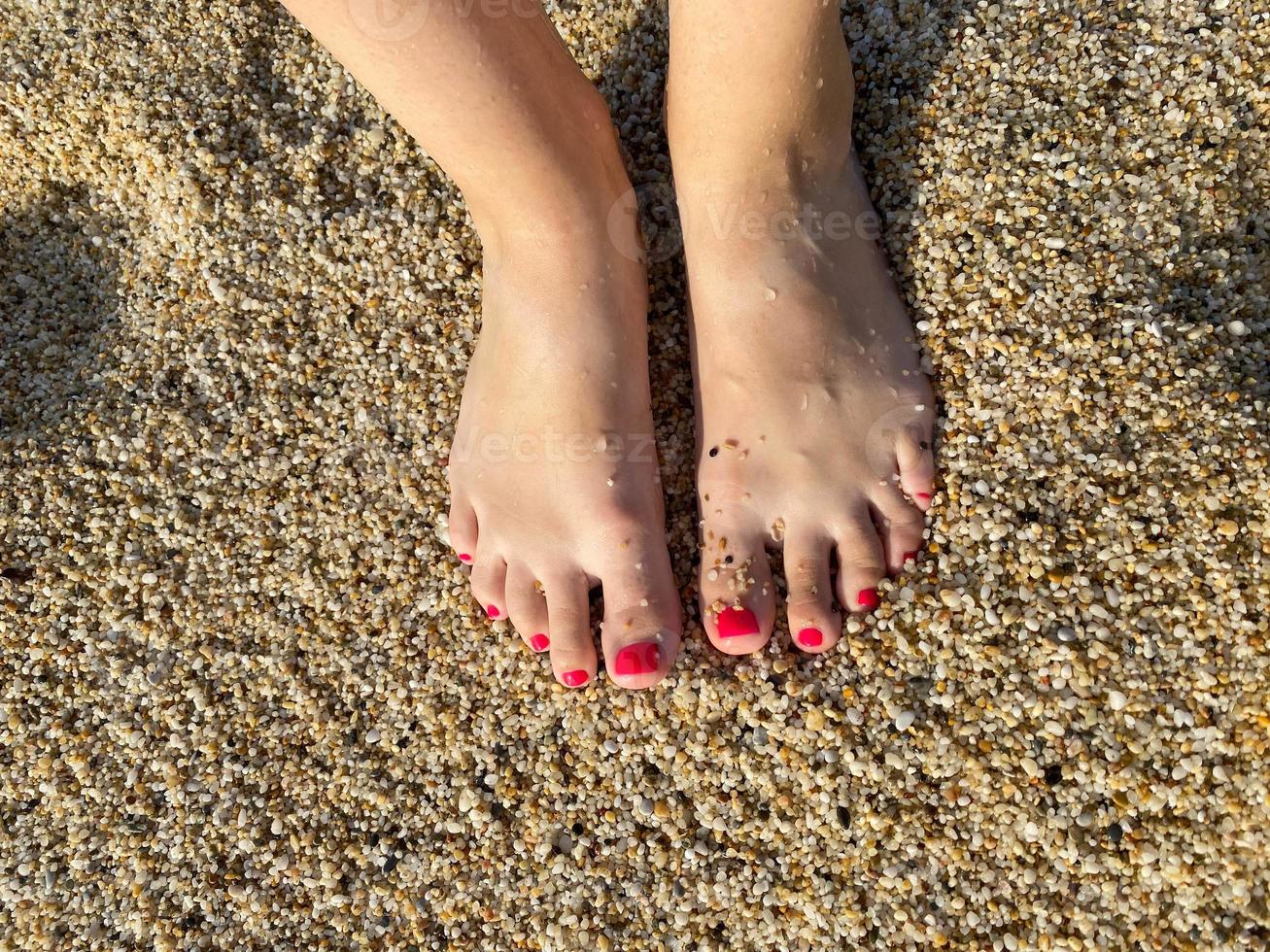 pernas femininas, pés com uma bela pedicure vermelha contra o fundo de areia dourada esfarelada de férias na praia em um resort tropical quente do paraíso oriental foto