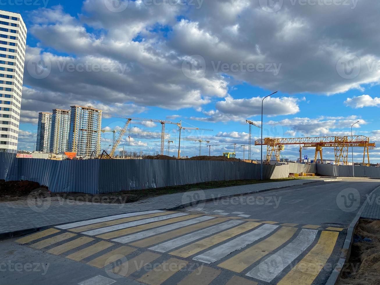 local de construção. grandes guindastes de torre industrial com edifícios altos inacabados e céu azul no fundo. andaime. engenharia civil moderna. paisagem urbana contemporânea foto