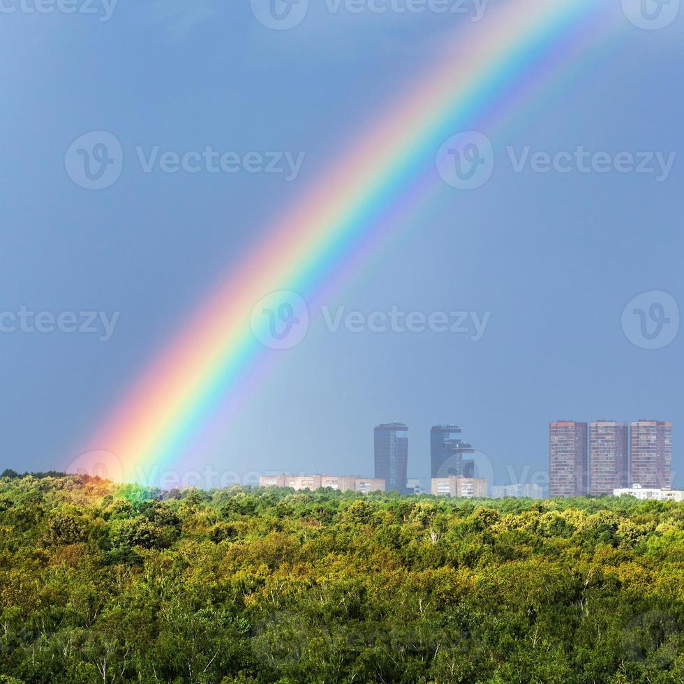 arco-íris no céu azul sobre a cidade e árvores verdes foto