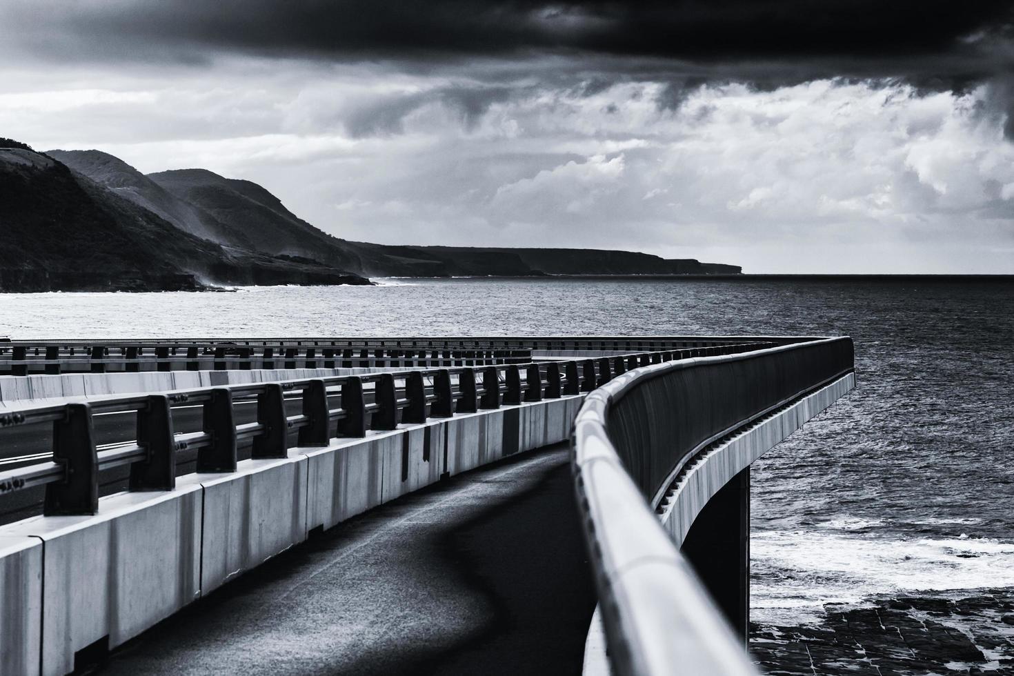 foto em tons de cinza de uma ponte sobre o oceano