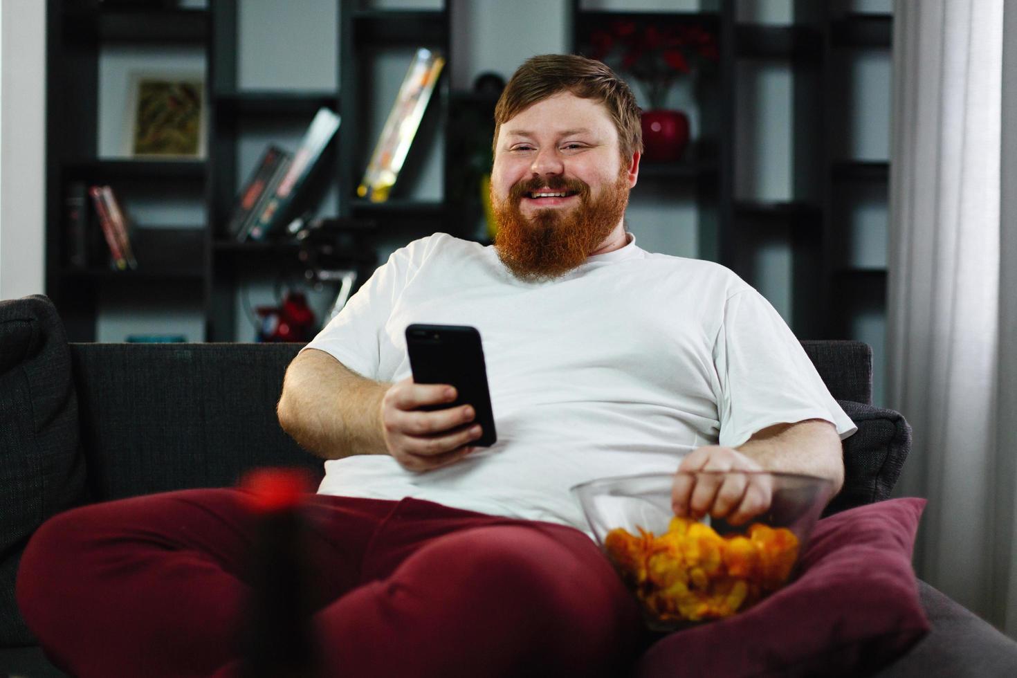 homem comendo batatinhas e jogando em seu telefone foto