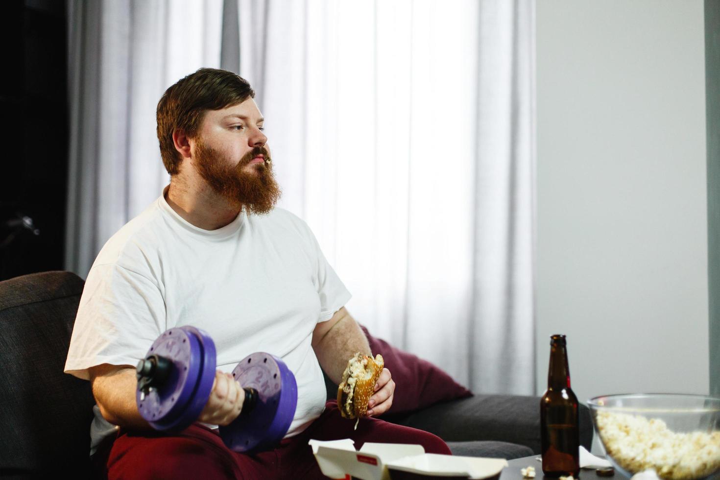 homem gordo se exercitando enquanto se senta para comer diante de um aparelho de TV foto