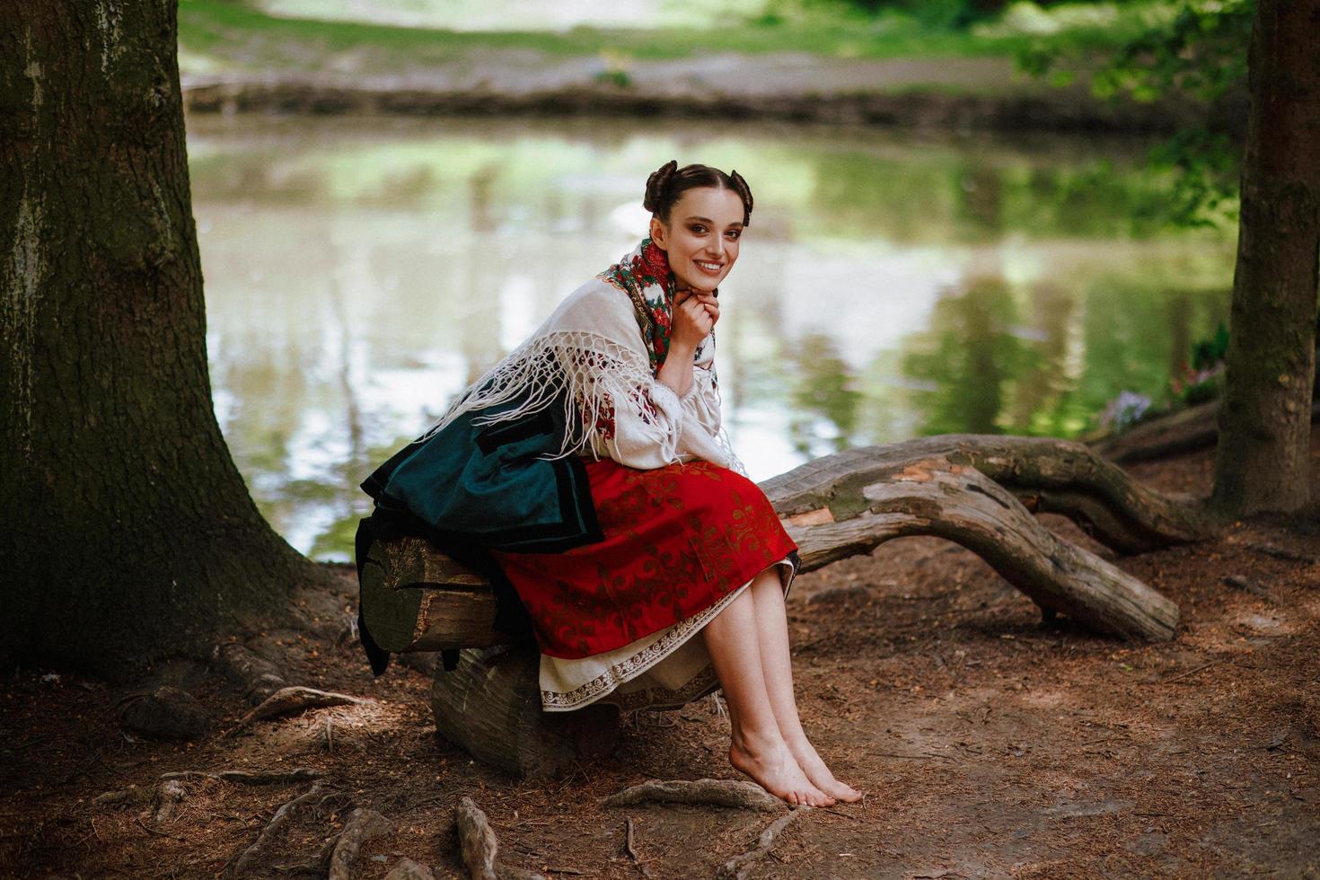 jovem com um vestido bordado étnico sentada em um banco perto do lago foto