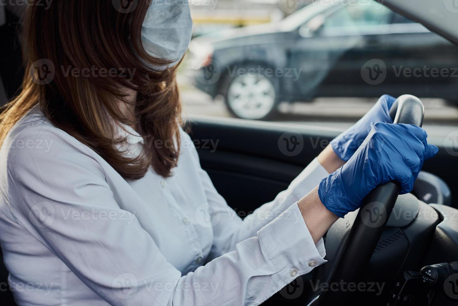 mulher com máscara protetora e luvas medicinais dirigindo um carro foto