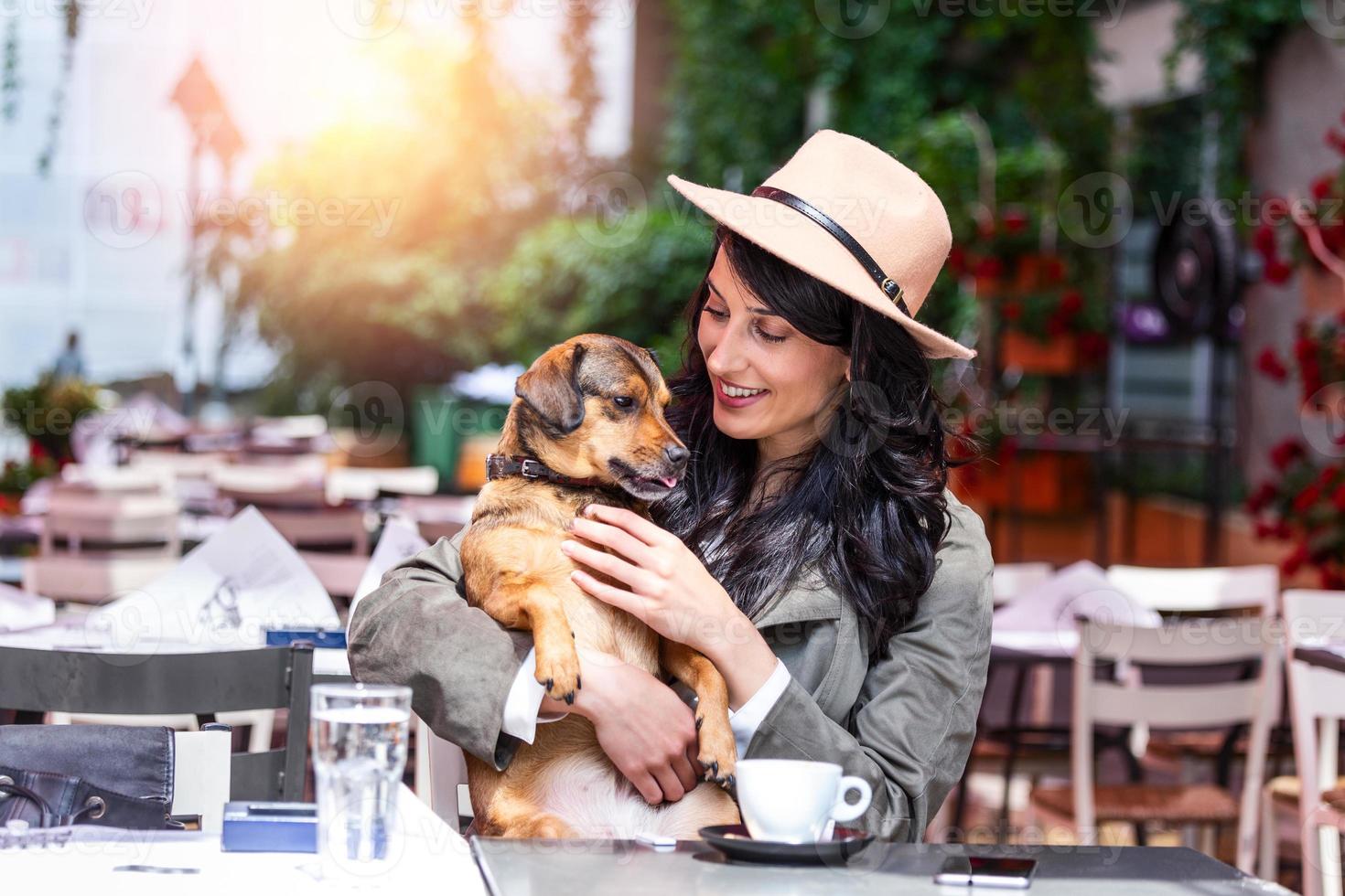 mulher jovem e atraente sentada na cafeteria, relaxando e segurando seu cachorro. cafeteria que aceita animais de estimação, linda garota com seu cachorro sentado em uma cafeteria e tomando café. foto