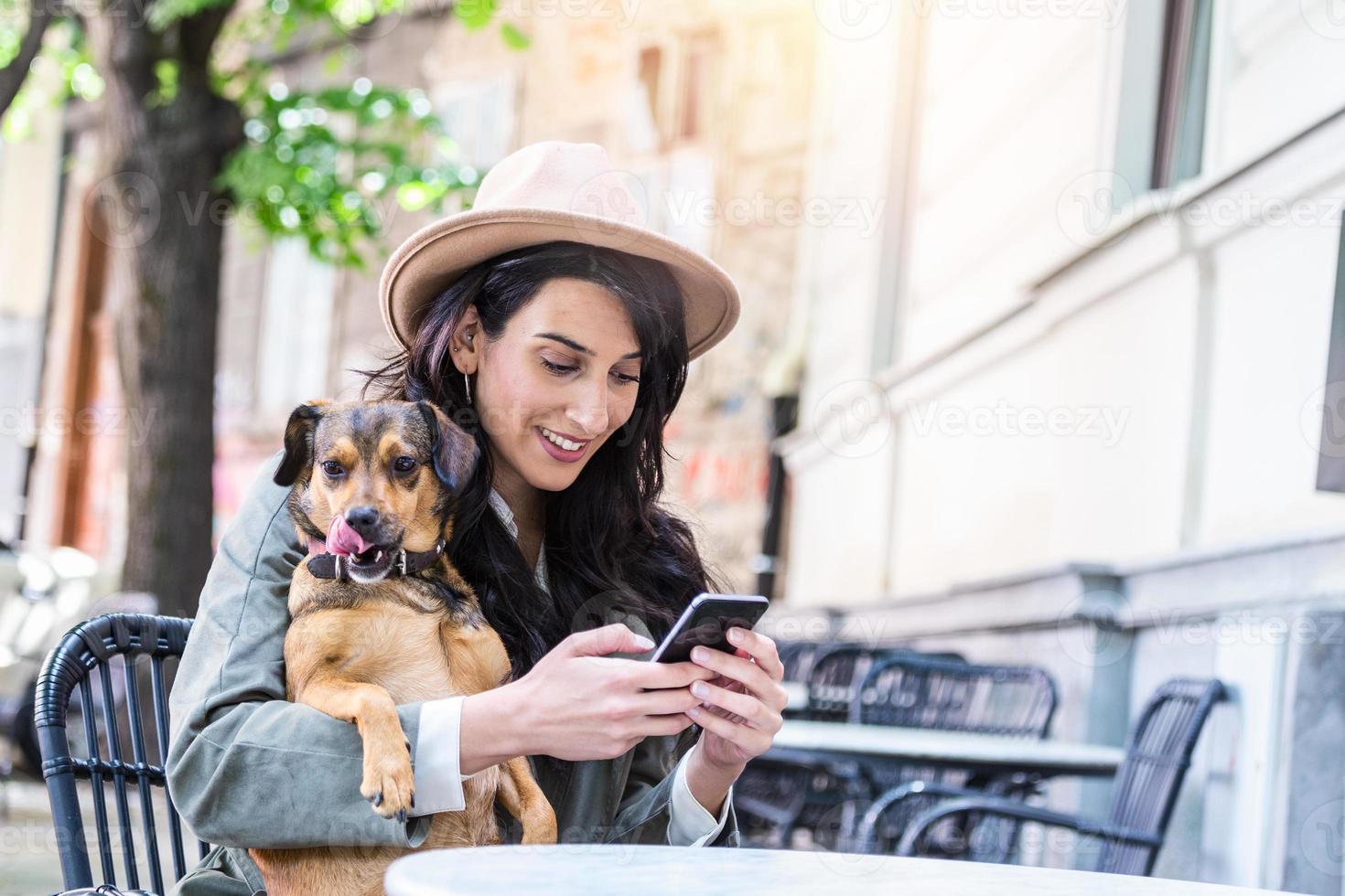 jovem mulher com seu cachorro em uma cafeteria que aceita animais de estimação. jovem mulher enviando mensagens de texto em seu celular enquanto relaxa no café durante o tempo livre com seu cachorro foto