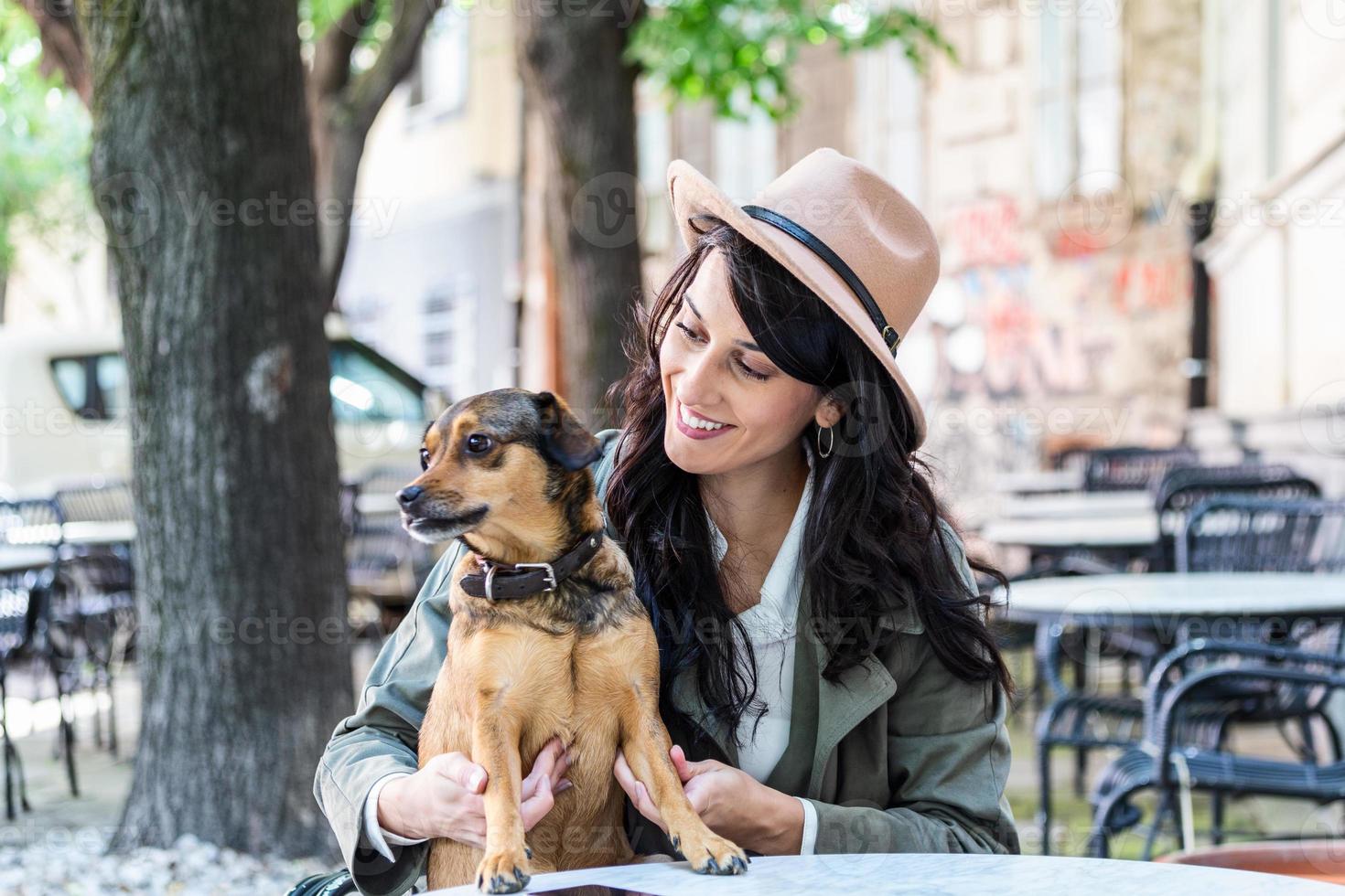 mulher jovem e atraente sentada na cafeteria, relaxando e segurando seu cachorro. cafeteria que aceita animais de estimação, linda garota com seu cachorro sentado em uma cafeteria e tomando café. foto