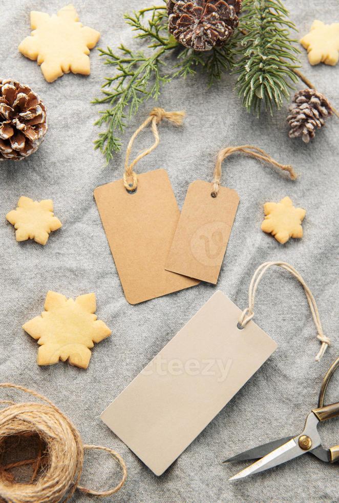 etiquetas de presente em branco com galho de pinheiro e biscoitos de natal em fundo têxtil. o conceito de preparação para o feriado de natal foto