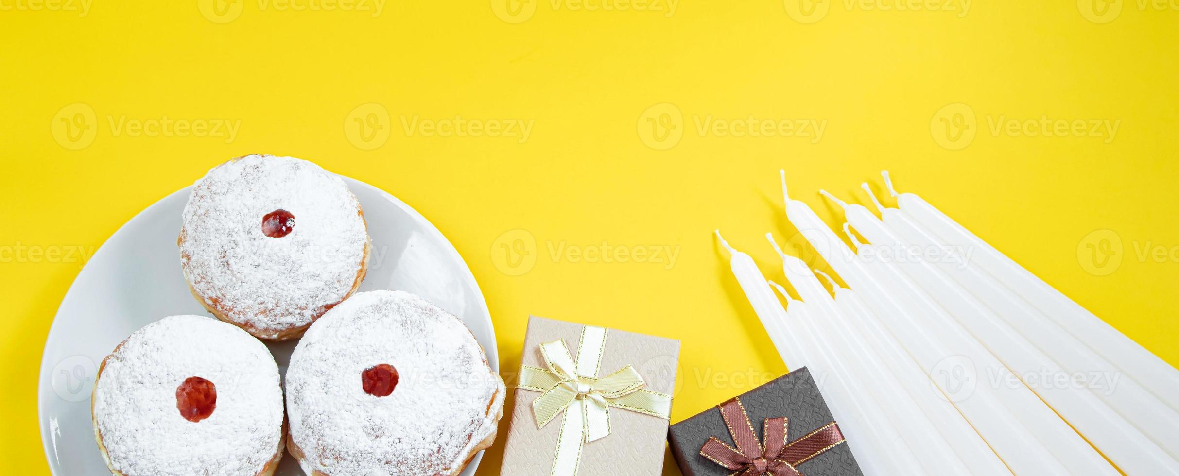 Feliz Hanukkah. sobremesa judaica sufganiyot em fundo amarelo. símbolos do feriado religioso do judaísmo. rosquinhas, velas e presente. foto