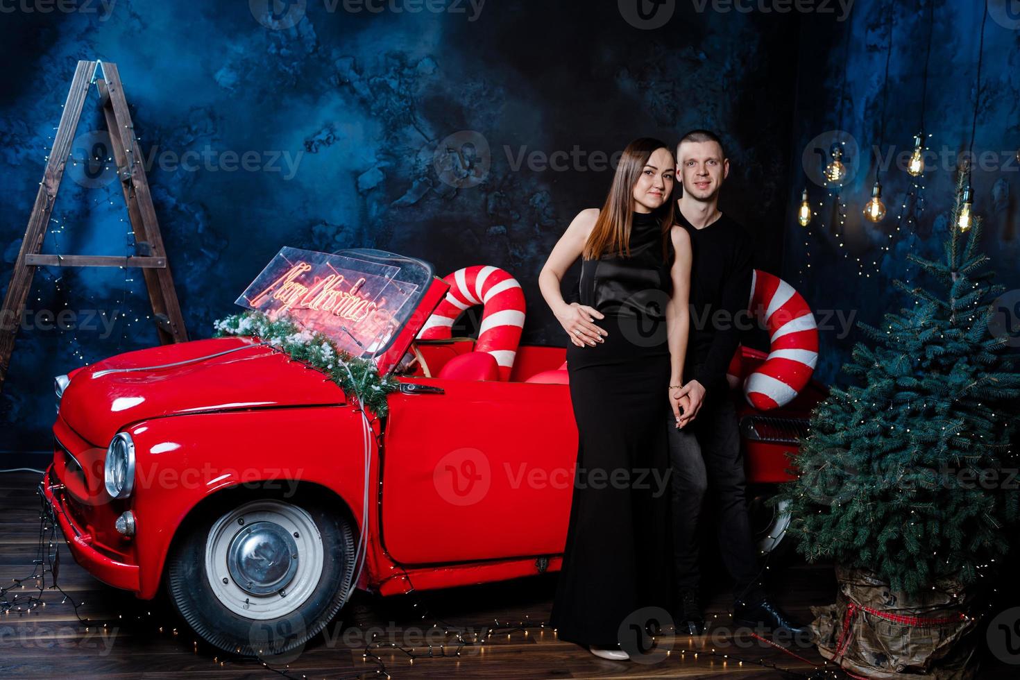 jovem casal feliz homem e mulher apaixonada no natal estão se abraçando perto de um carro retrô vermelho com presentes de ano novo. beijo, menina, felicidade, celebração de natal em quarentena, feriado. foto