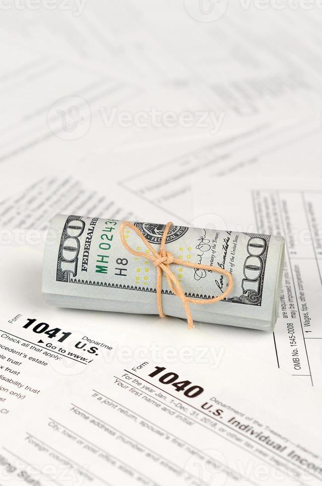 formulários fiscais fica perto de um rolo de notas de cem dólares. restituição do Imposto de Renda foto
