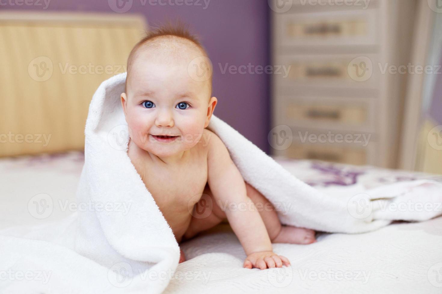 lindo bebê sorridente olhando para a câmera sob uma toalha branca. retrato de uma criança fofa foto