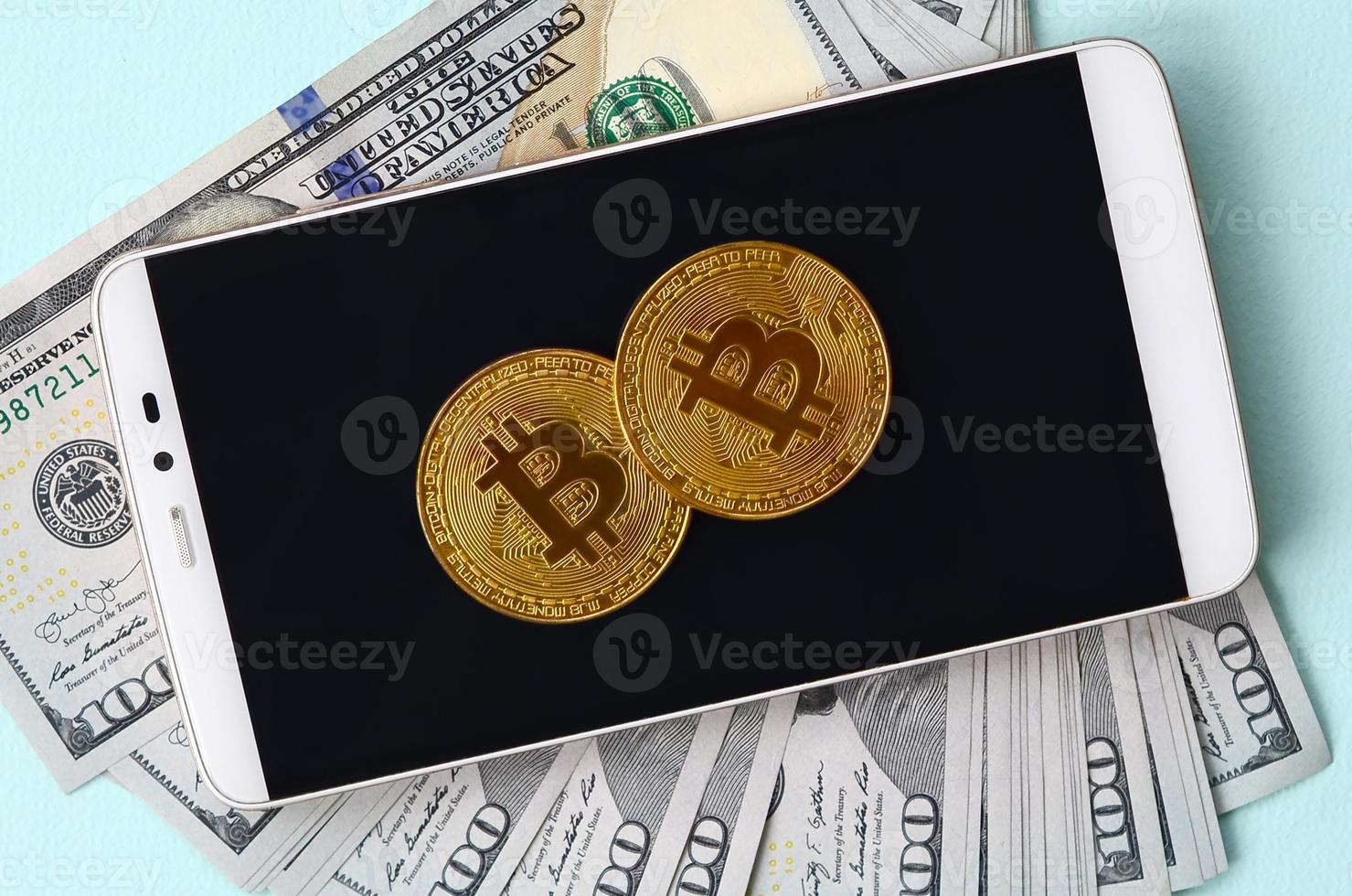 bitcoins está em um smartphone e notas de cem dólares em um fundo azul claro foto