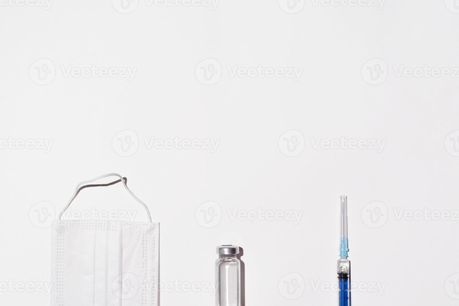 ampola, máscara facial médica e seringa em um fundo branco, copie o espaço. conceito de vacinação de vista superior. foto