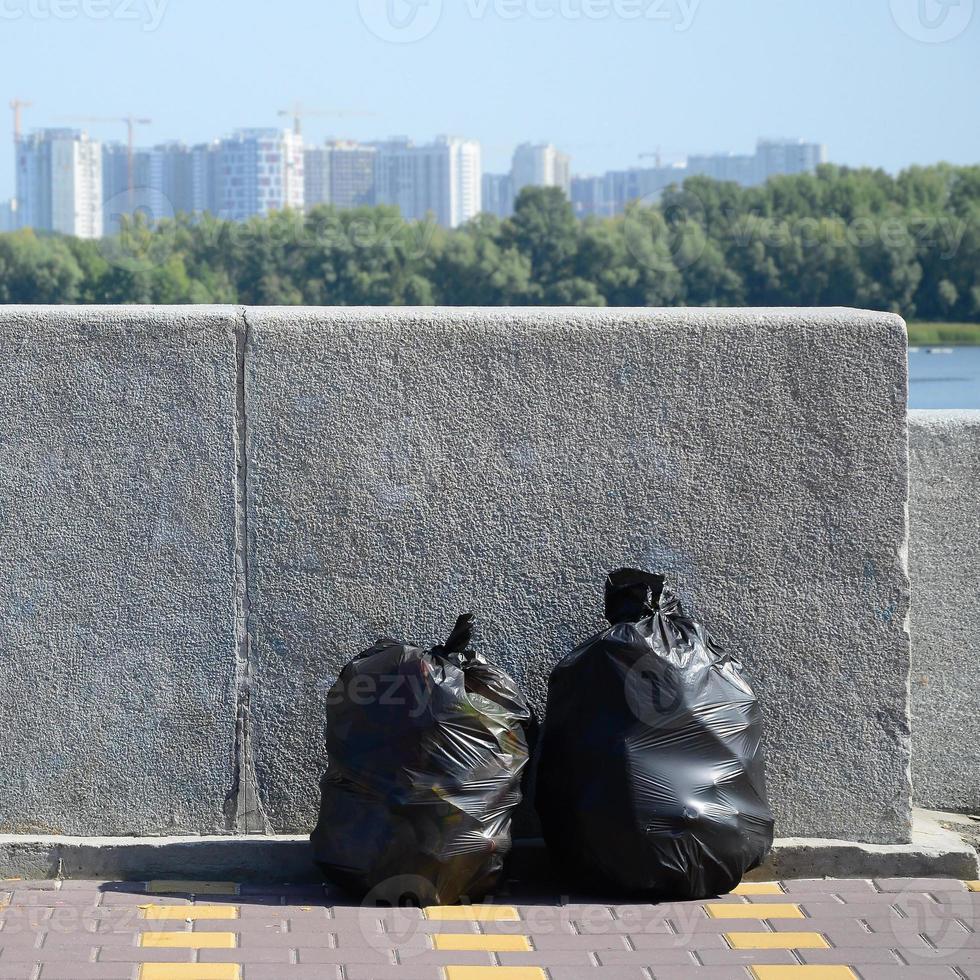 dois sacos de lixo pretos no chão da rua de azulejos na cerca de concreto na cidade foto