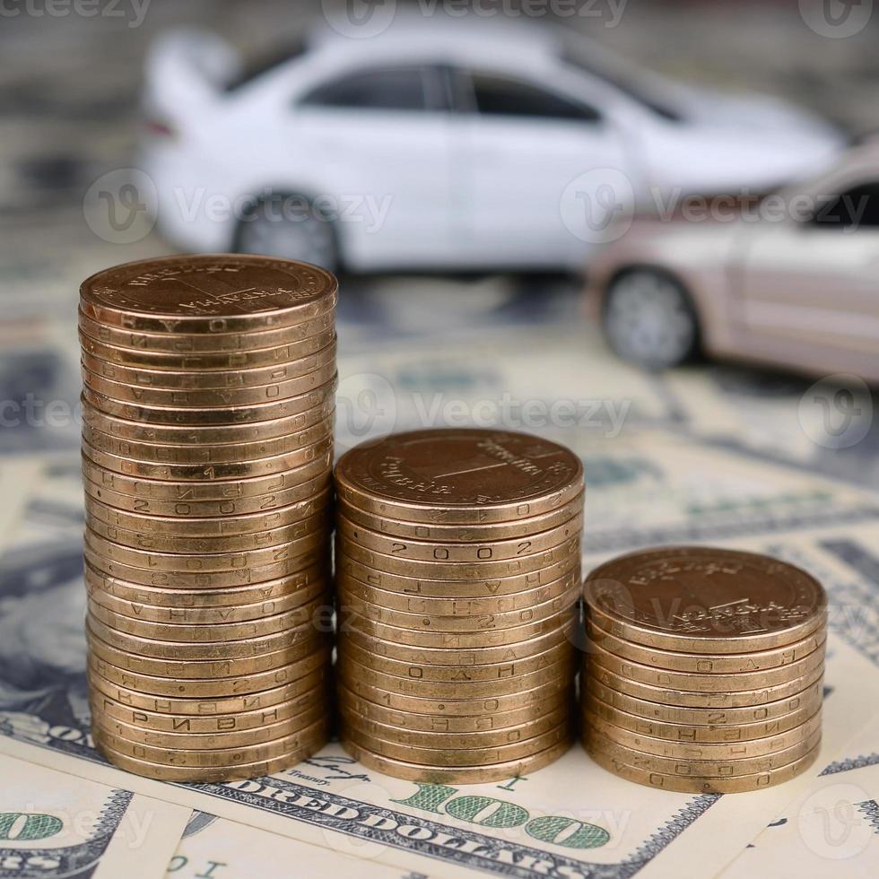 carro de brinquedo em acidente em um fundo de notas de 100 dólares e pilhas de moedas de ouro foto