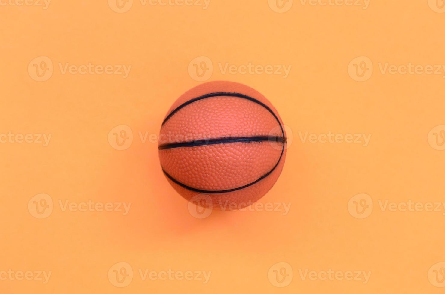 pequena bola laranja para jogo de esporte de basquete encontra-se no fundo de textura de papel de cor laranja pastel de moda em conceito mínimo foto