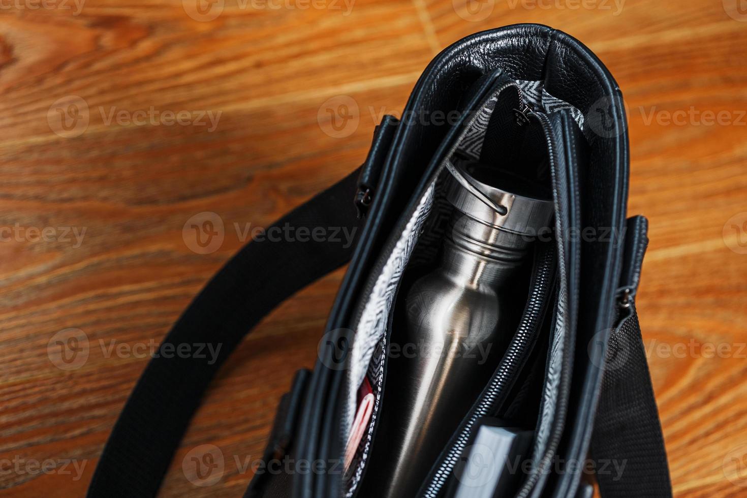 um caderno preto e uma garrafa estão no bolso de um close-up de uma bolsa de couro preto, macro feito à mão, materiais naturais. foto