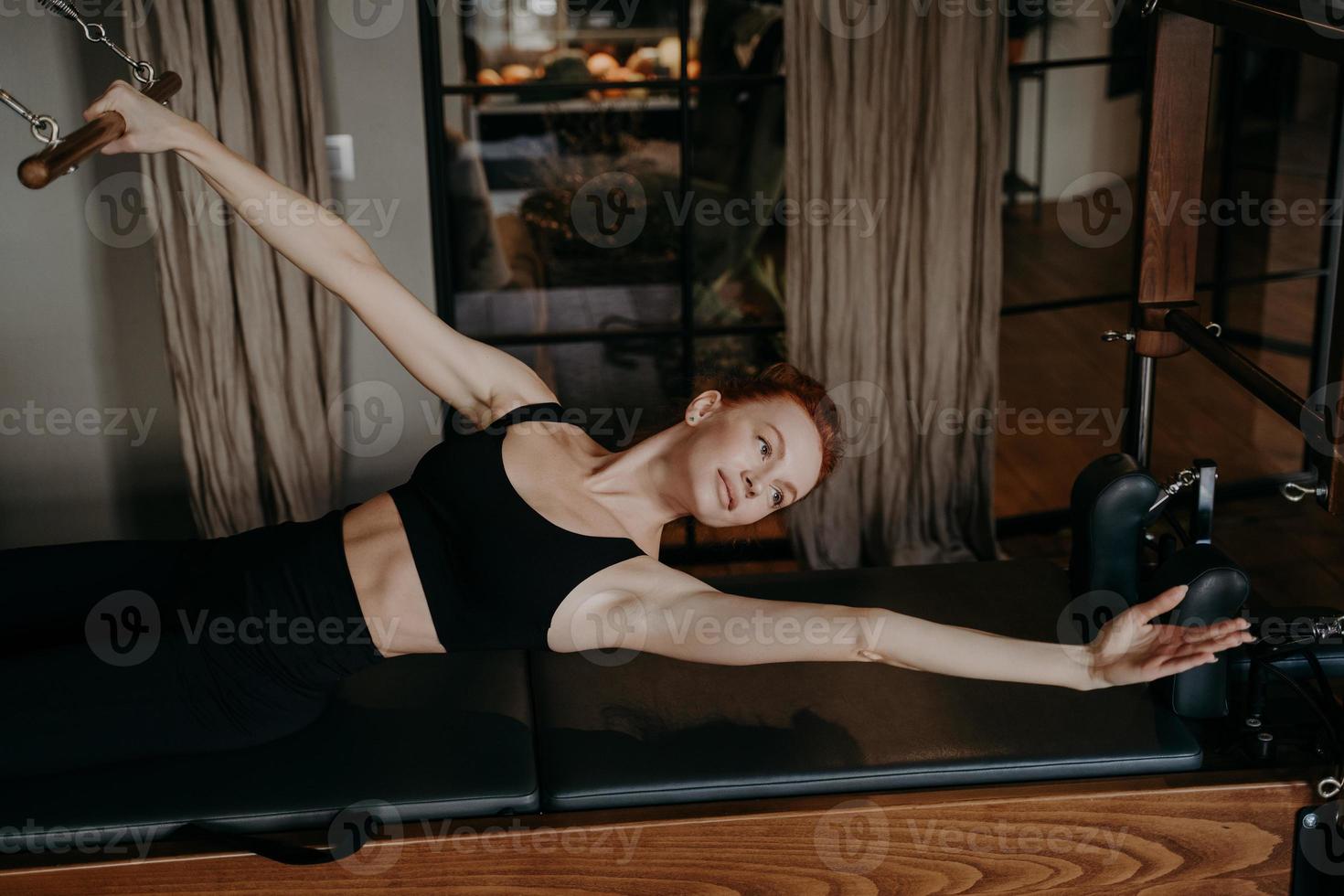 instrutor de pilates feminino jovem deitado na posição de braço esticado no reformador cadillac foto