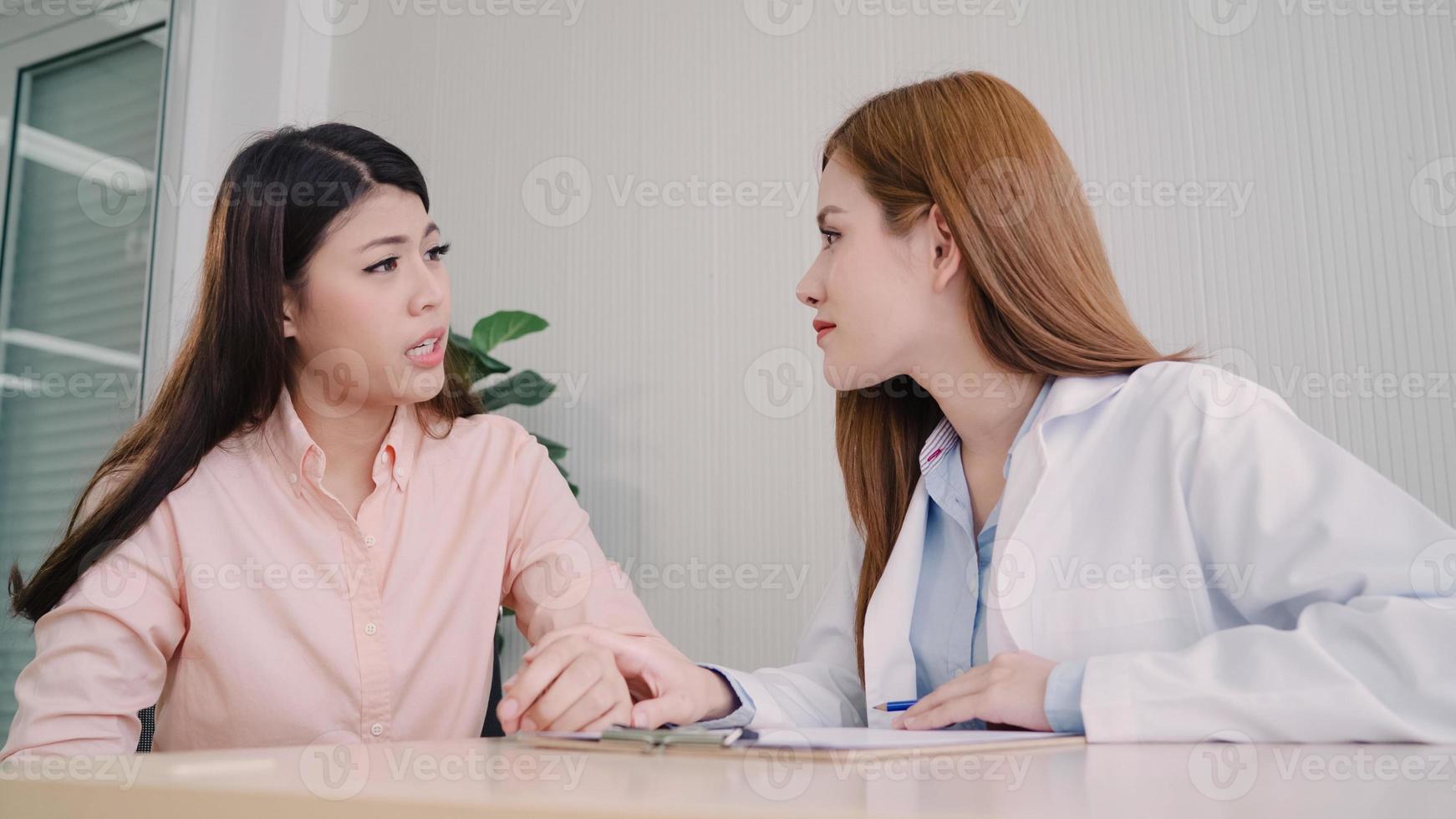 médico falando com paciente adolescente infeliz na sala de exames. mulher asiática encorajamento médico e apoio ao paciente com câncer após consultar e examinar a saúde na clínica médica ou hospital. foto