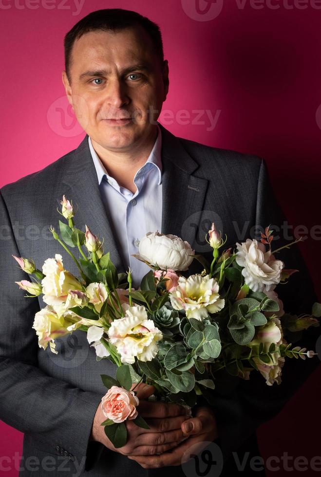 empresário bonito de terno olha para a câmera com um buquê de flores. foto