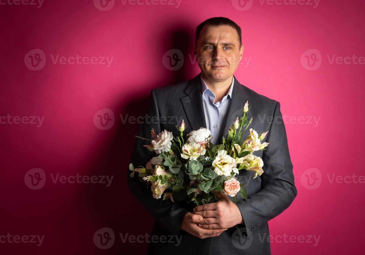empresário bonito de terno olha para a câmera com um buquê de flores. foto