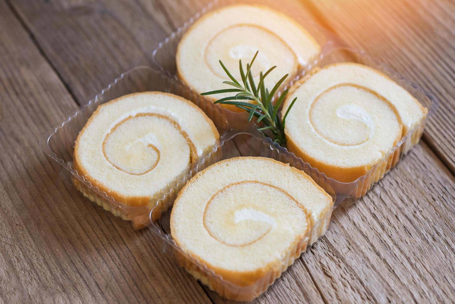 rolo de bolo em bolo de caixa com alecrim em madeira, fatias de rolo de pão de ló doces sobremesa rolo de creme lanches de baunilha e conceito de comida - bolo de rocambole foto