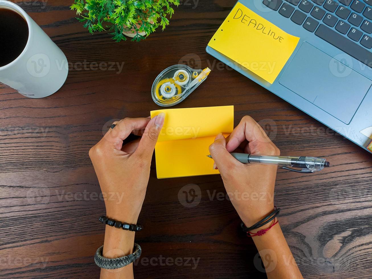 as mulheres escrevem em notas amarelas, simulam notas amarelas. as mãos das mulheres escrevem notas em papel de nota amarelo no fundo do espaço de trabalho da mesa de escritório da vista superior. foto