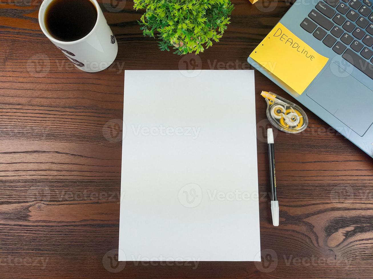 configuração plana, maquete de papel. espaço de trabalho no fundo da mesa de escritório da vista superior. com papel branco em branco, laptops, material de escritório, lápis, folhas verdes e xícaras de café foto