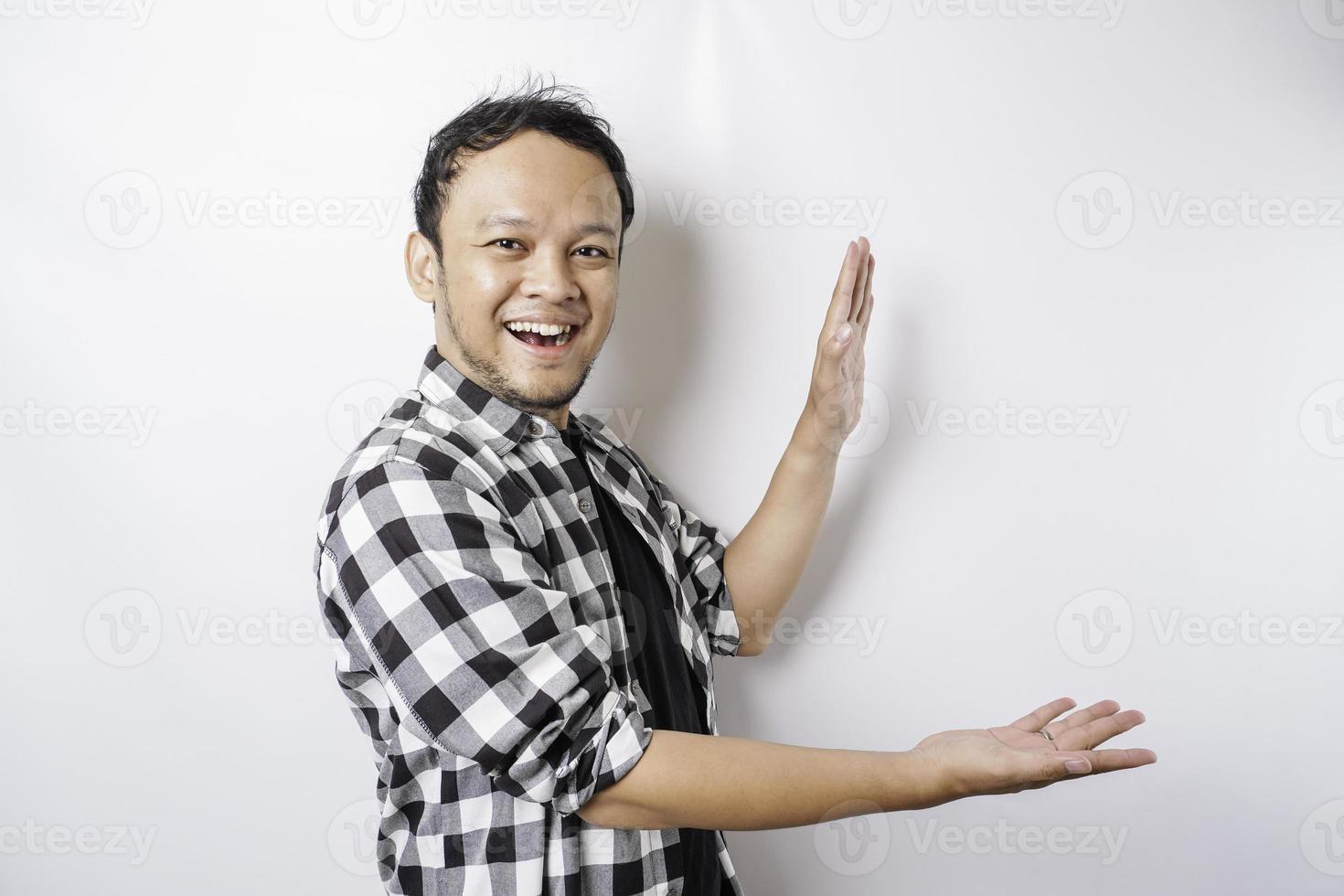 homem asiático animado vestindo camisa xadrez está apontando para o espaço da cópia ao lado dele, isolado pelo fundo branco foto