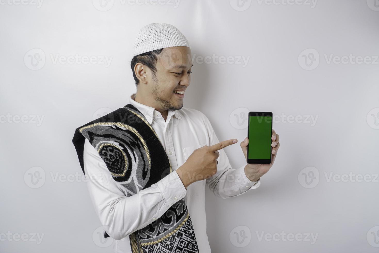 um retrato de um homem muçulmano asiático feliz sorrindo enquanto mostra o espaço da cópia em seu telefone, isolado pelo fundo branco foto