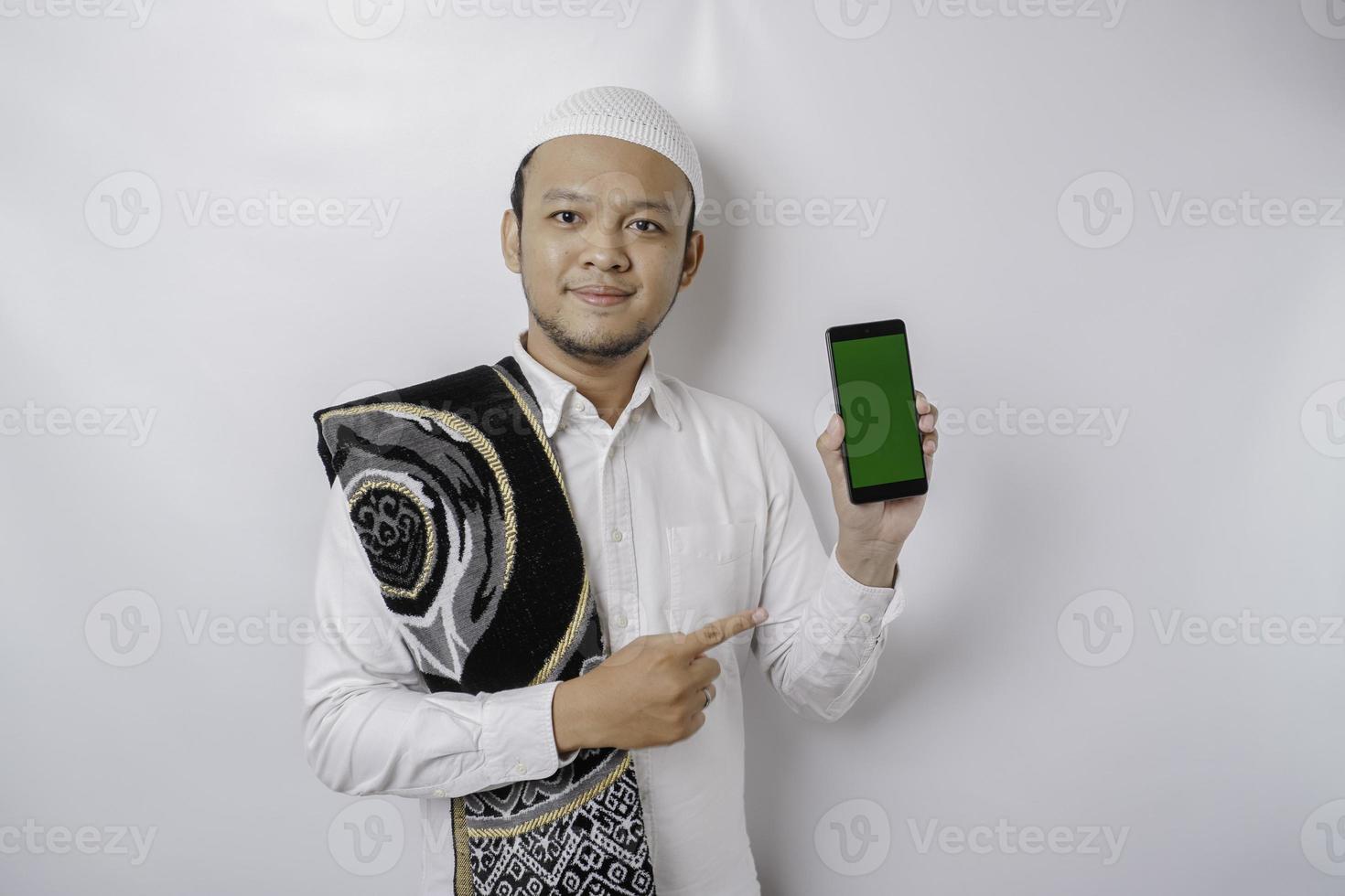 um retrato de um homem muçulmano asiático feliz sorrindo enquanto mostra o espaço da cópia em seu telefone, isolado pelo fundo branco foto