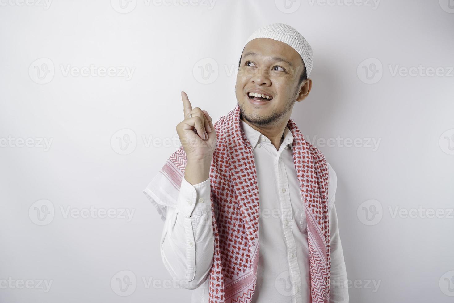 homem muçulmano asiático animado apontando para o espaço da cópia ao lado dele, isolado pelo fundo branco foto