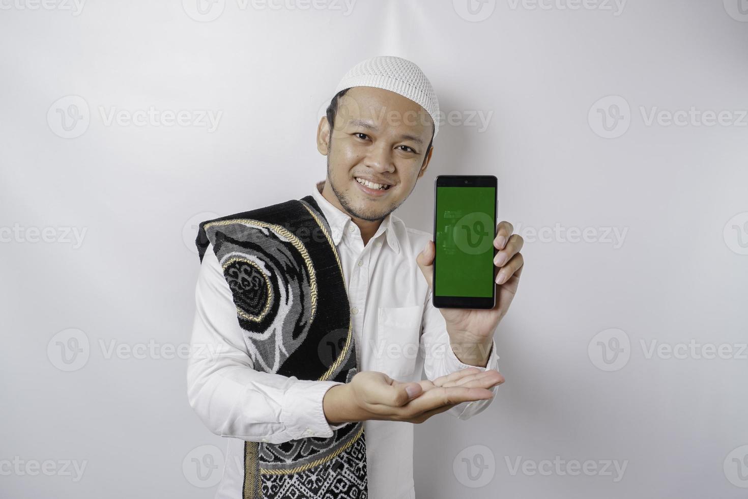 um retrato de um homem muçulmano asiático feliz sorrindo enquanto mostra o espaço da cópia em seu telefone, isolado pelo fundo branco foto