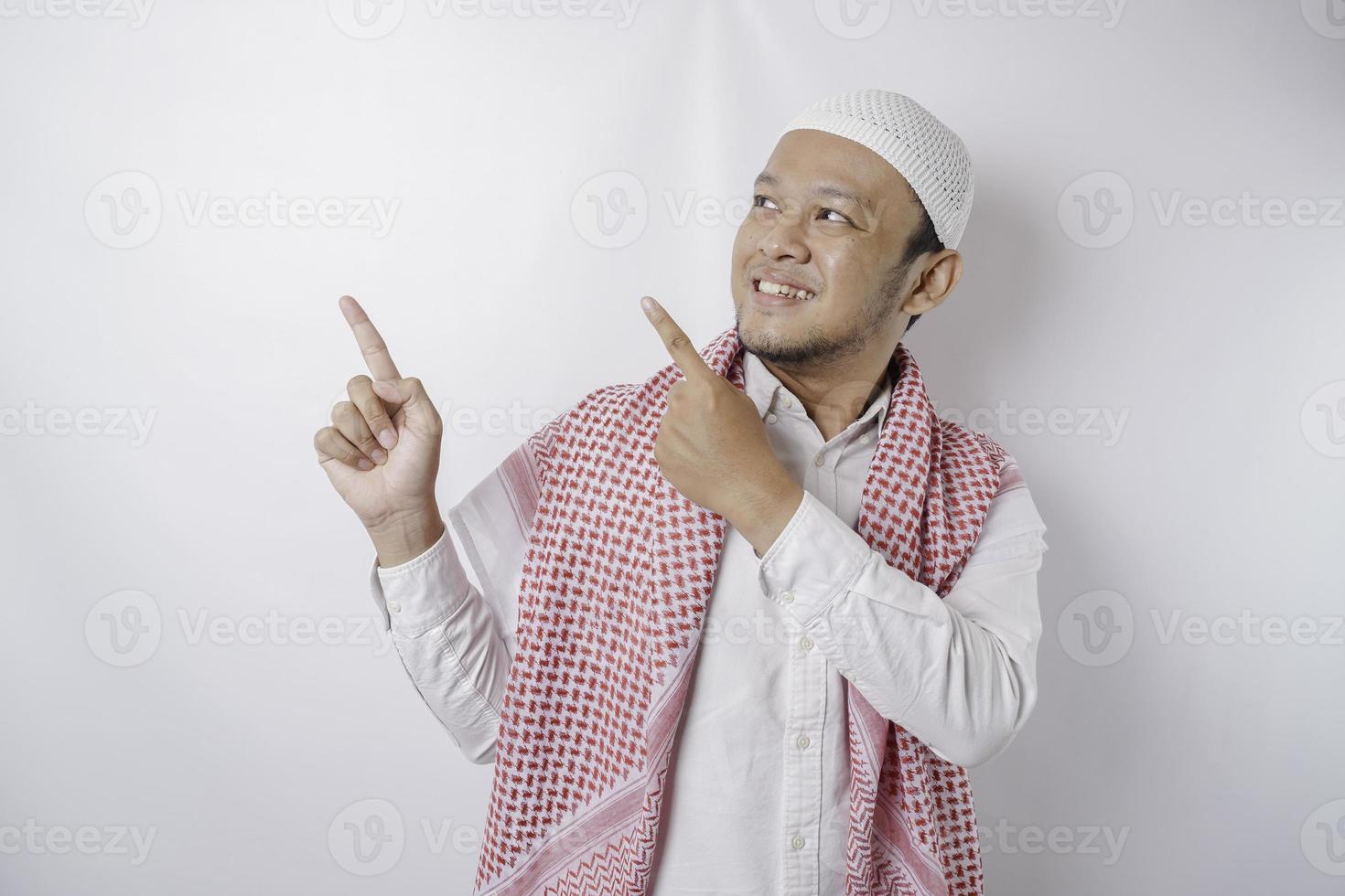 homem muçulmano asiático animado apontando para o espaço da cópia ao lado dele, isolado pelo fundo branco foto