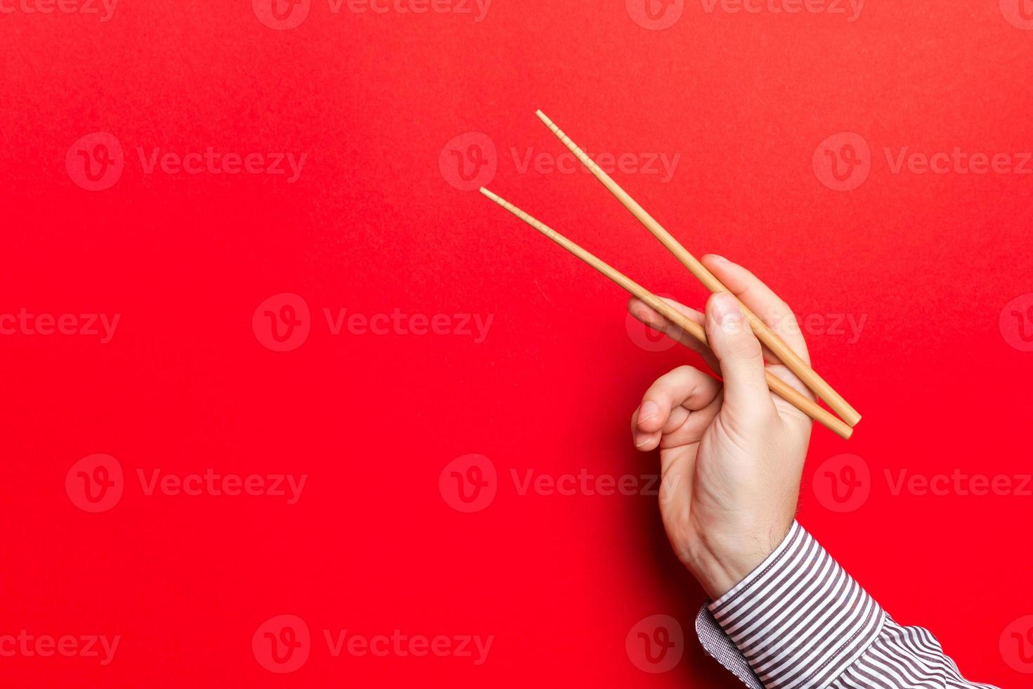 mão masculina com pauzinhos em fundo vermelho. comida asiática tradicional com espaço vazio para seu projeto foto