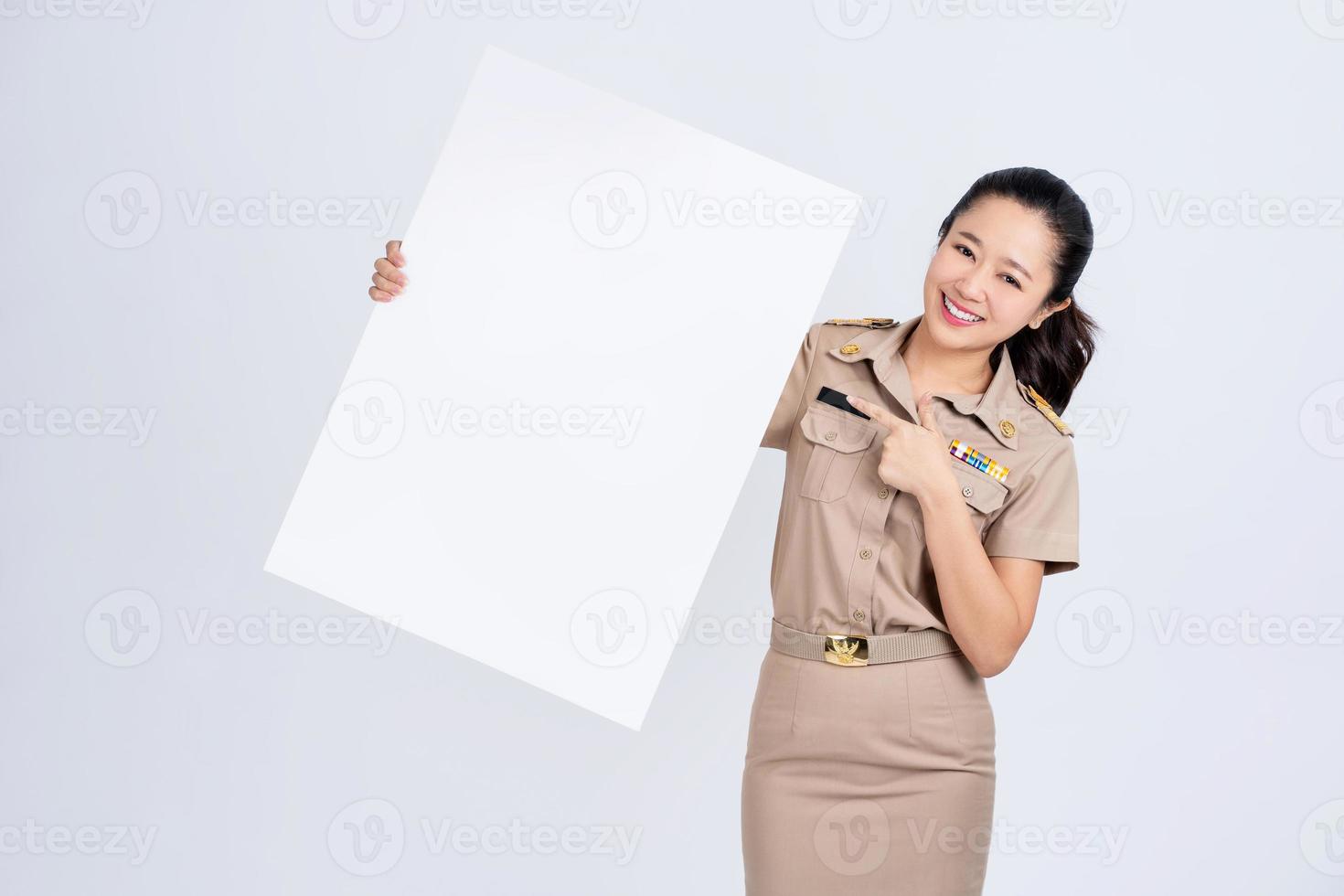 jovem mulher asiática em roupas de trabalho de uniforme marrom, ela mostrando e segurando outdoor branco em branco foto