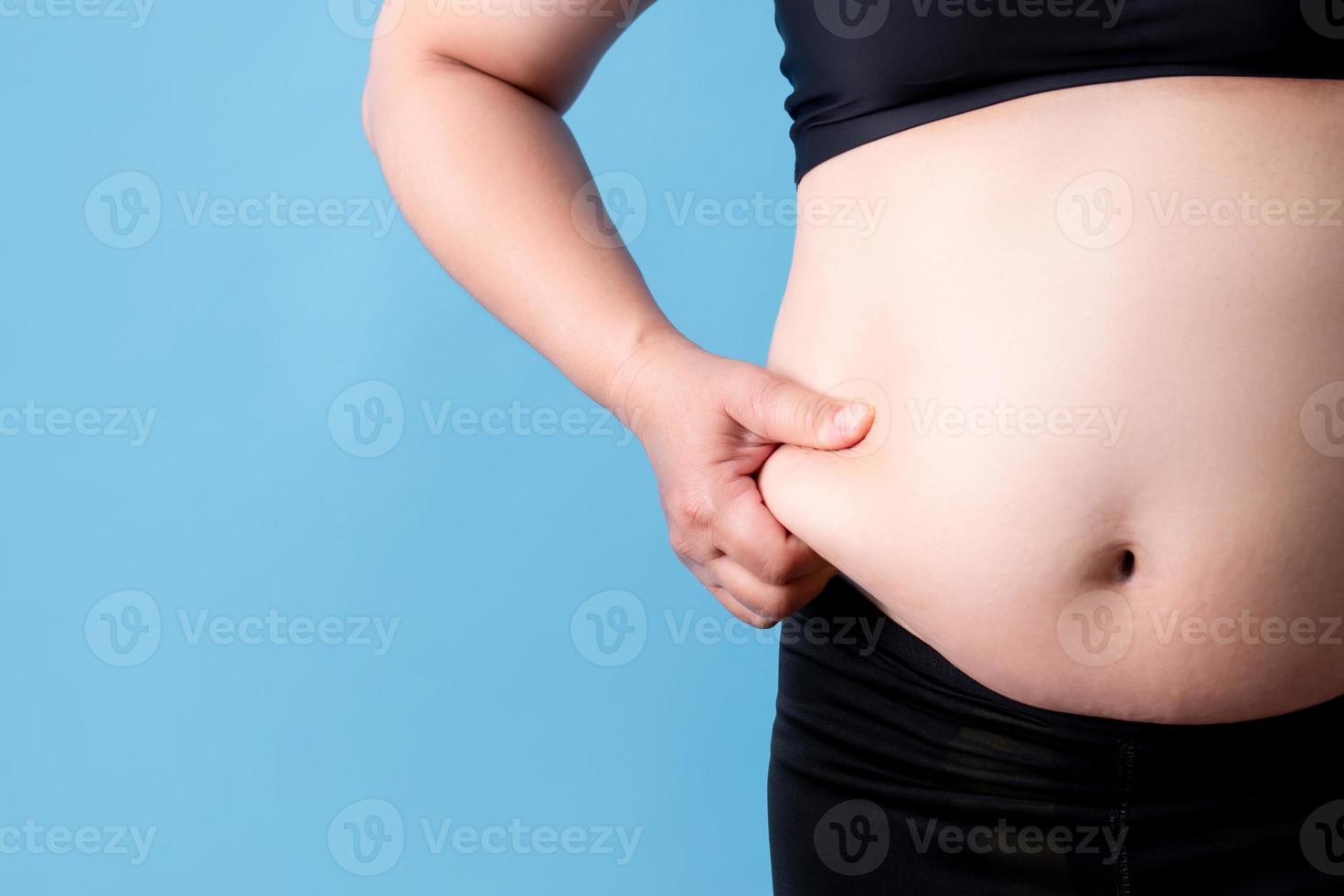 mulher com sobrepeso pega gordura na barriga em um fundo azul. fundo isolado foto