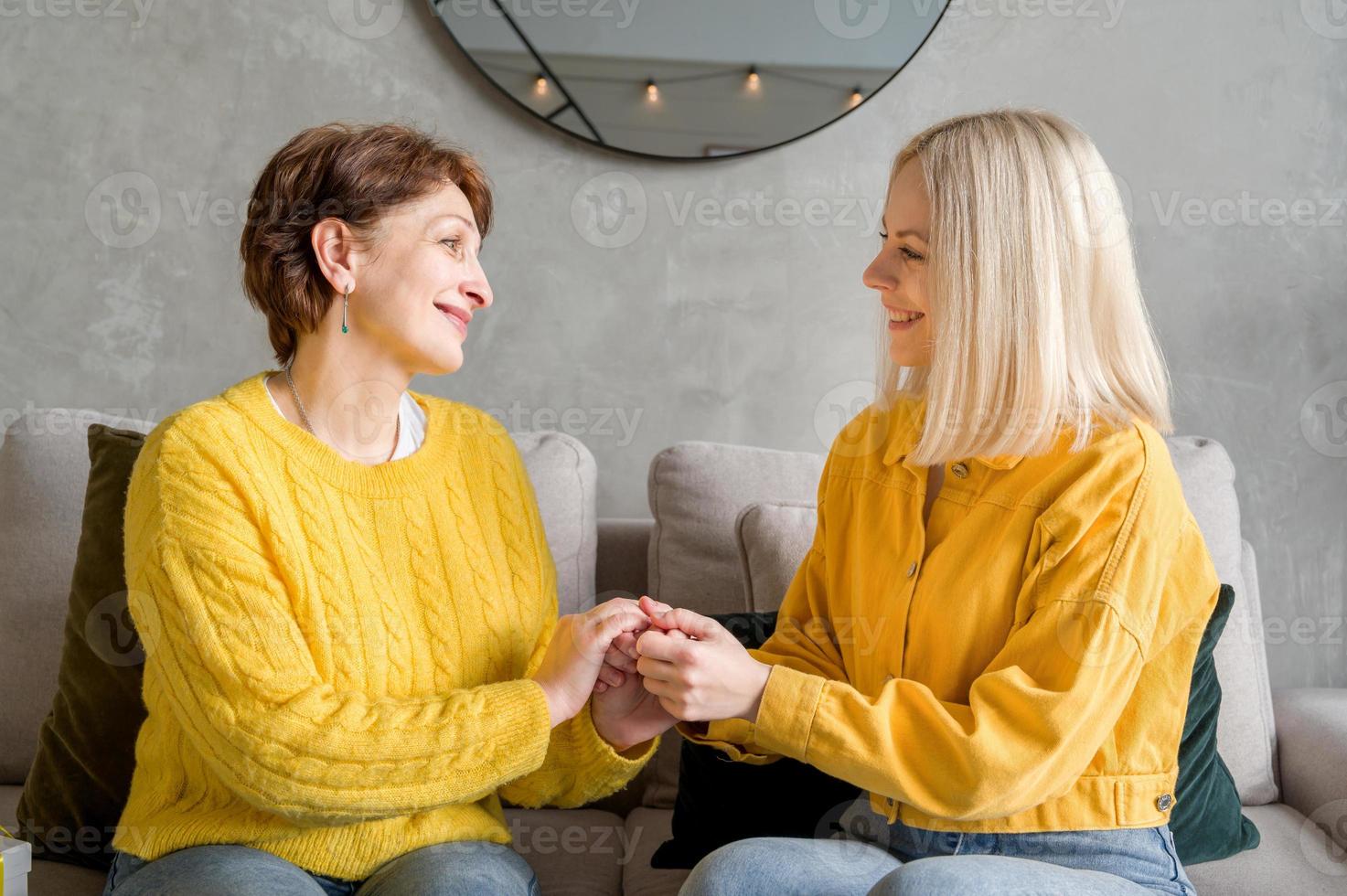 filha adulta feliz se comunicando com a mãe dela, sentados juntos no sofá. foto