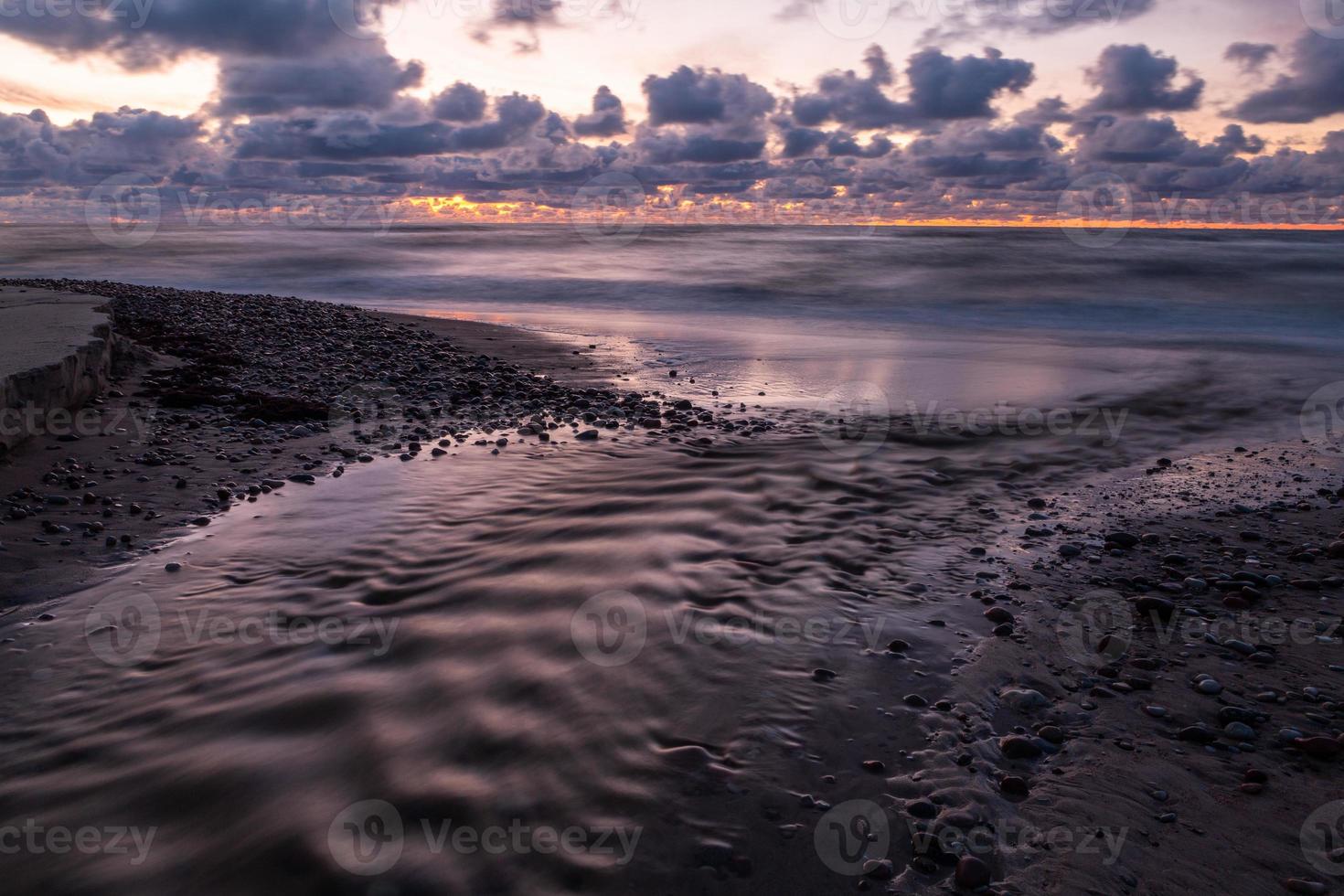 costa do mar báltico com seixos e gelo ao pôr do sol foto