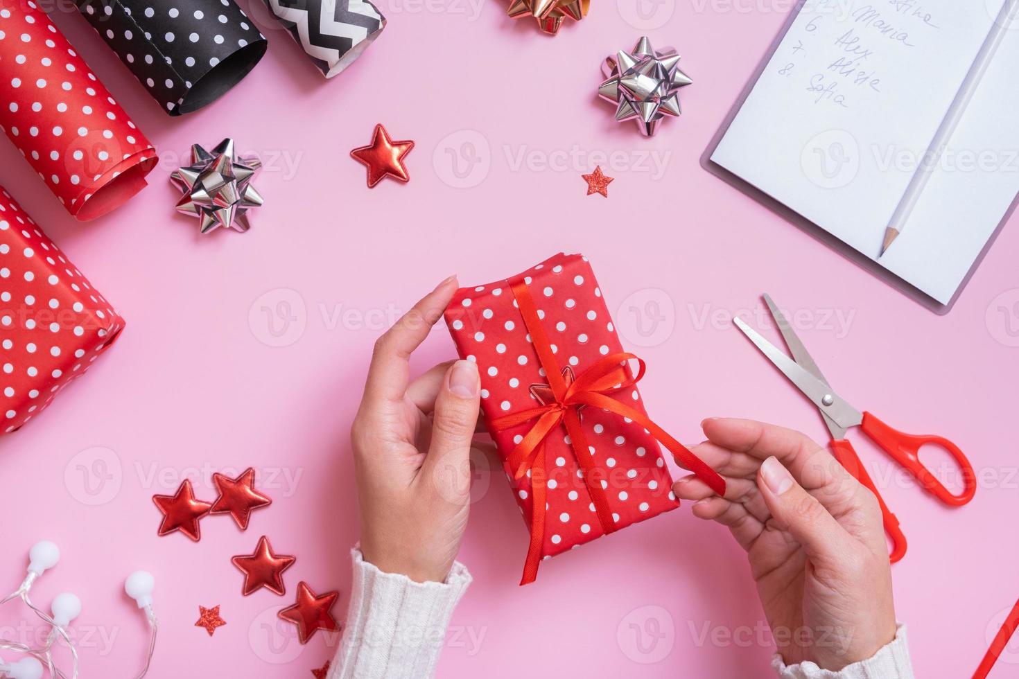 mãos femininas embrulhando presentes de natal planas sobre fundo rosa. preparação de natal vista superior foto