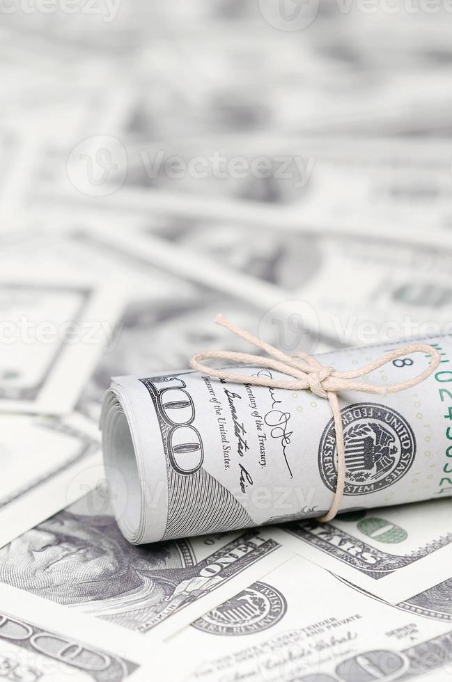 dólares americanos enrolados e apertados com banda estão em muitas notas americanas com fundo desfocado foto
