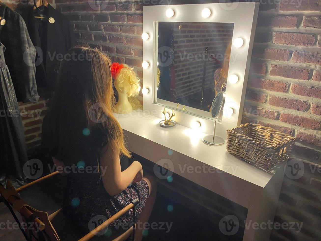 mulher se maquiando em frente ao espelho no camarim vista de trás foto