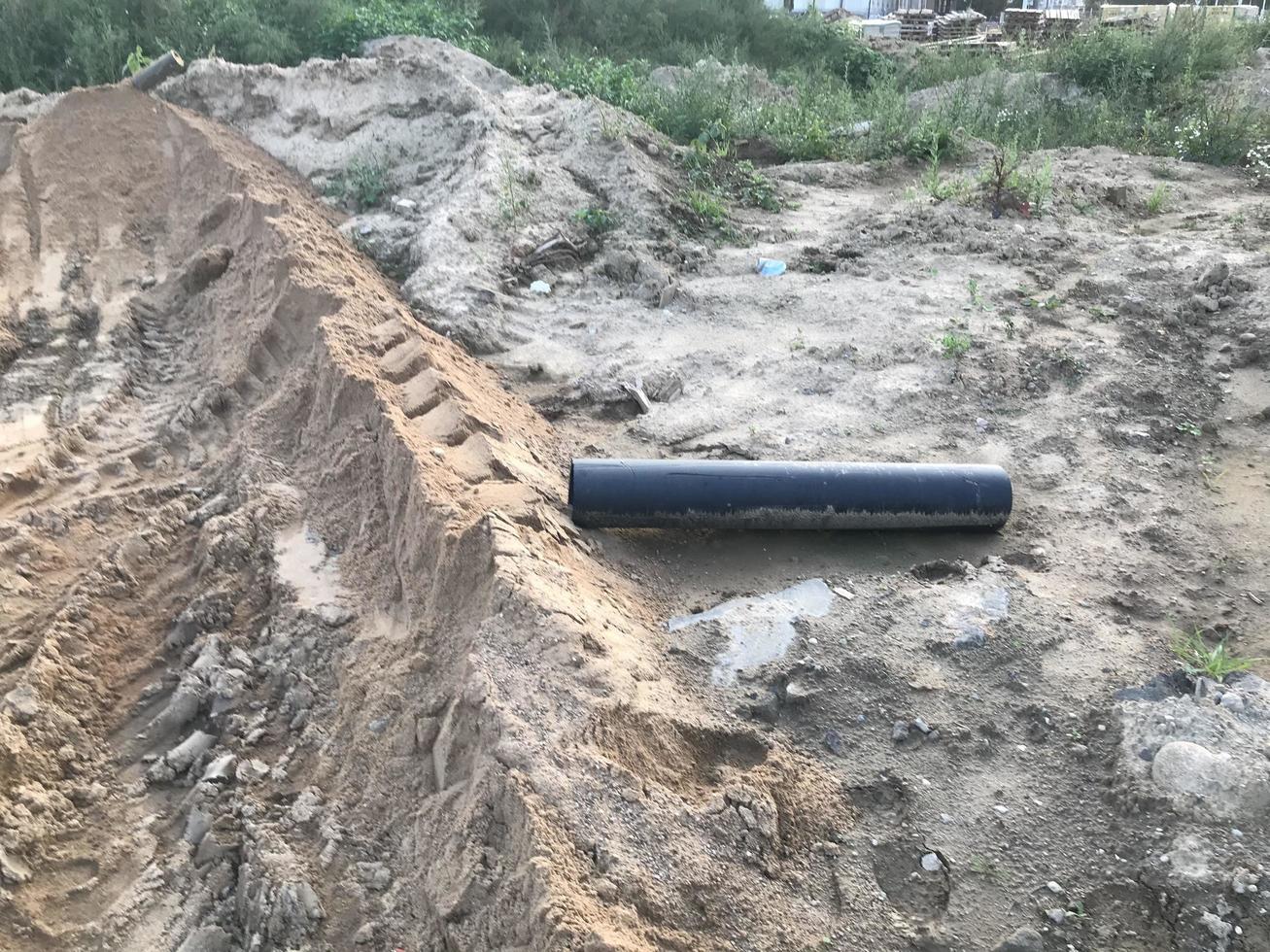 sujeira em um canteiro de obras. sulcos de areia de tratores e pavimentadoras. sulcos de areia, rastros de veículos pesados. há um tubo de plástico próximo, estabelecendo comunicações para casas foto