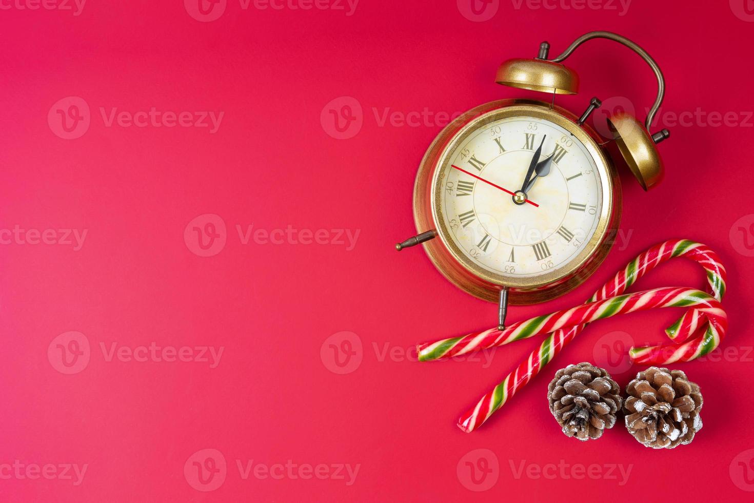 despertador de bronze, bastão de doces e cones de abeto sobre fundo vermelho. plano de fundo natal e ano novo foto