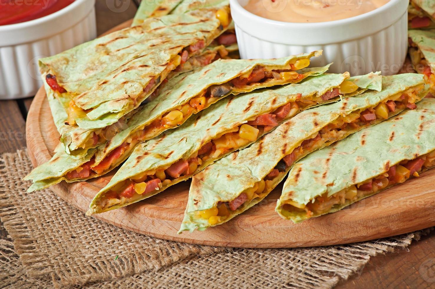 quesadilla mexicano fatiado com legumes e molhos em cima da mesa foto