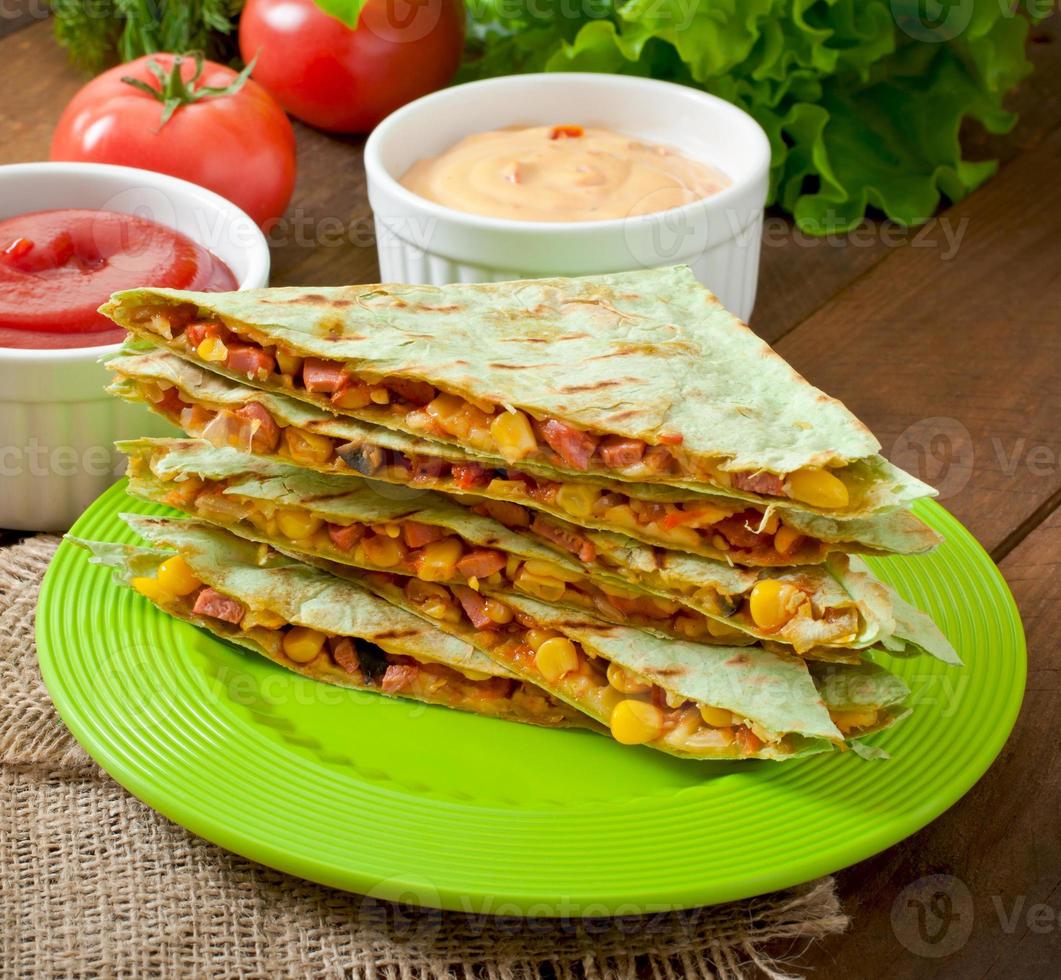 quesadilla mexicano fatiado com legumes e molhos em cima da mesa foto