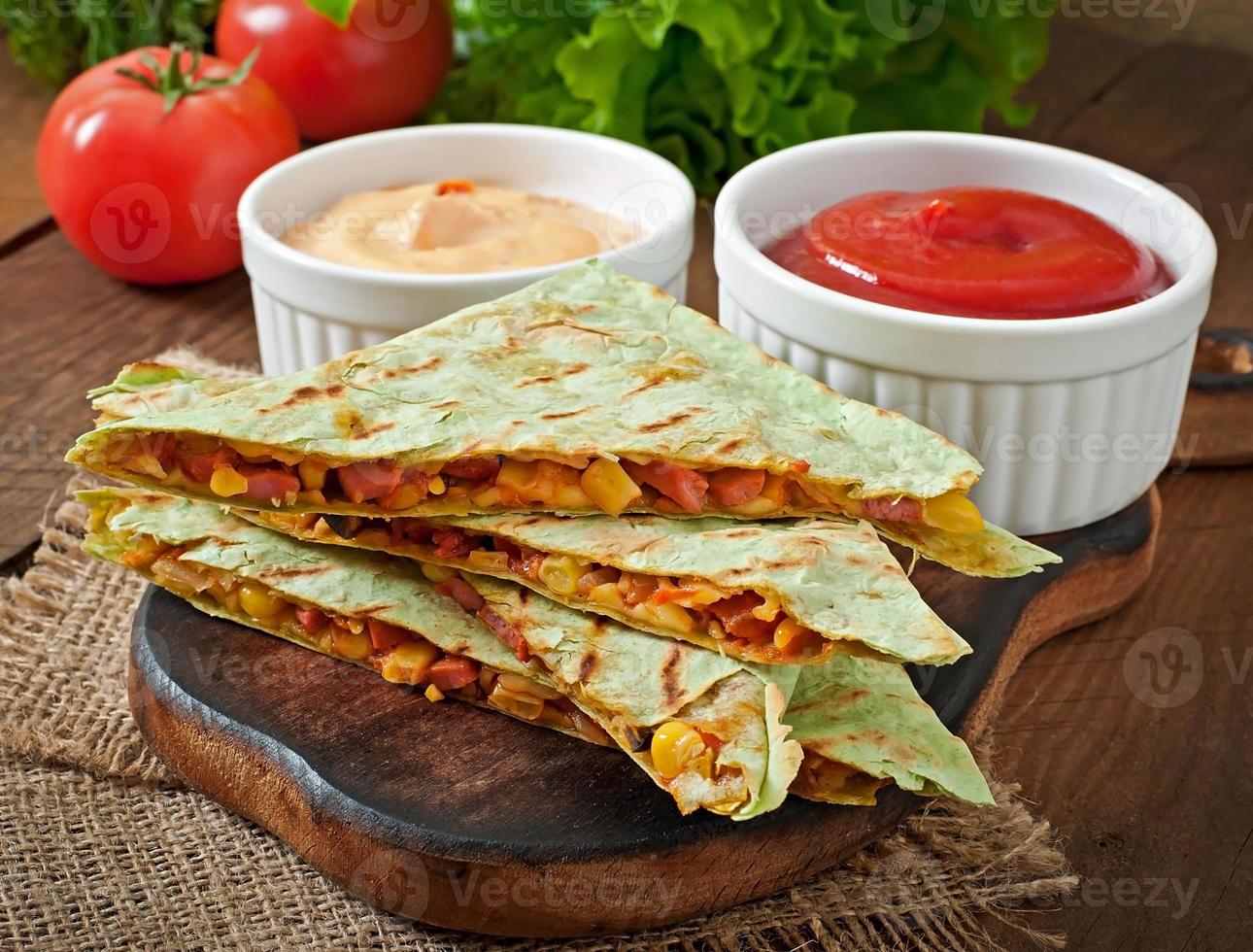 quesadilla mexicano fatiado com legumes e molhos em cima da mesa foto