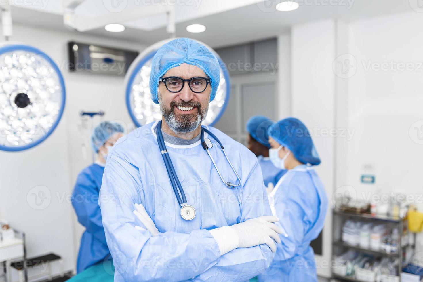 retrato do cirurgião masculino em pé com os braços cruzados no teatro de operação no hospital. cirurgiões da equipe estão realizando uma operação, médico de meia-idade está olhando para a câmera, em uma sala de cirurgia moderna foto