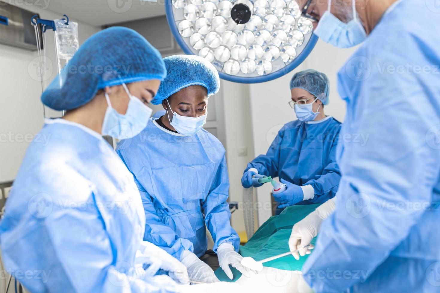 grupo de cirurgiões usando máscaras de segurança realizando operação. conceito de medicina. conceito de cirurgia, medicina e pessoas - grupo de cirurgiões em operação na sala de cirurgia do hospital foto